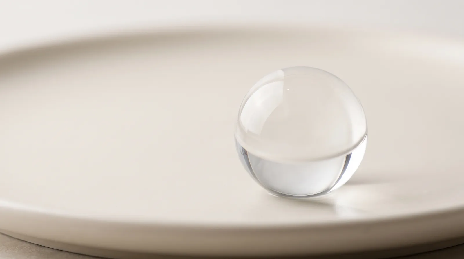 Translucent Hyaluronic Acid hydro-gel sphere resting on a matte ivory ceramic plate