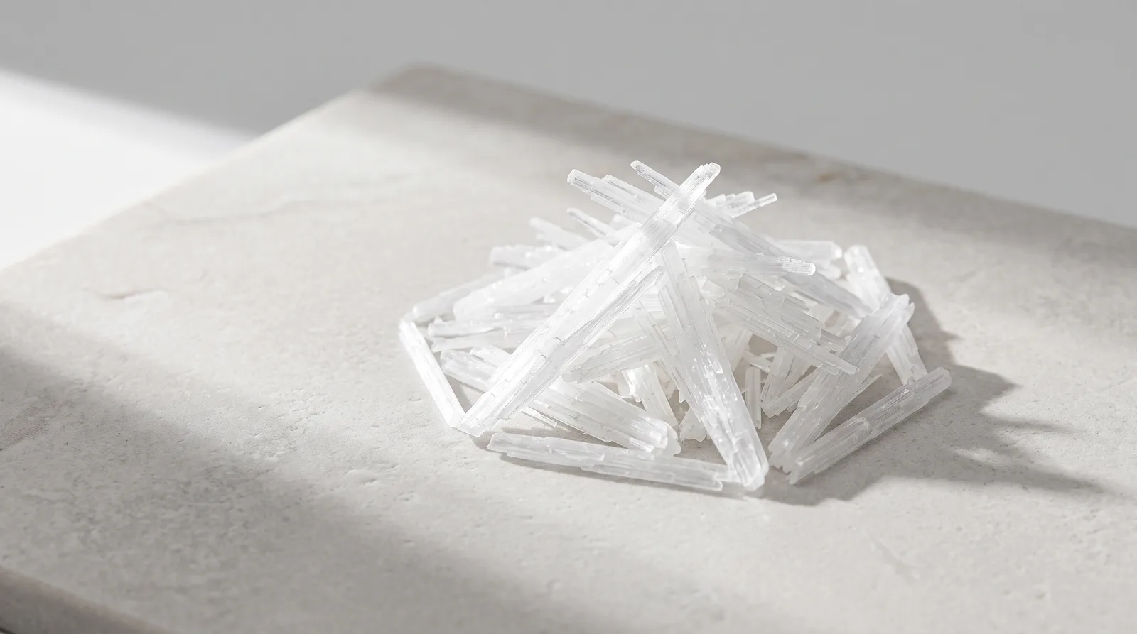 Cluster of pure Niacinamide crystals resting on pale grey limestone with soft morning daylight