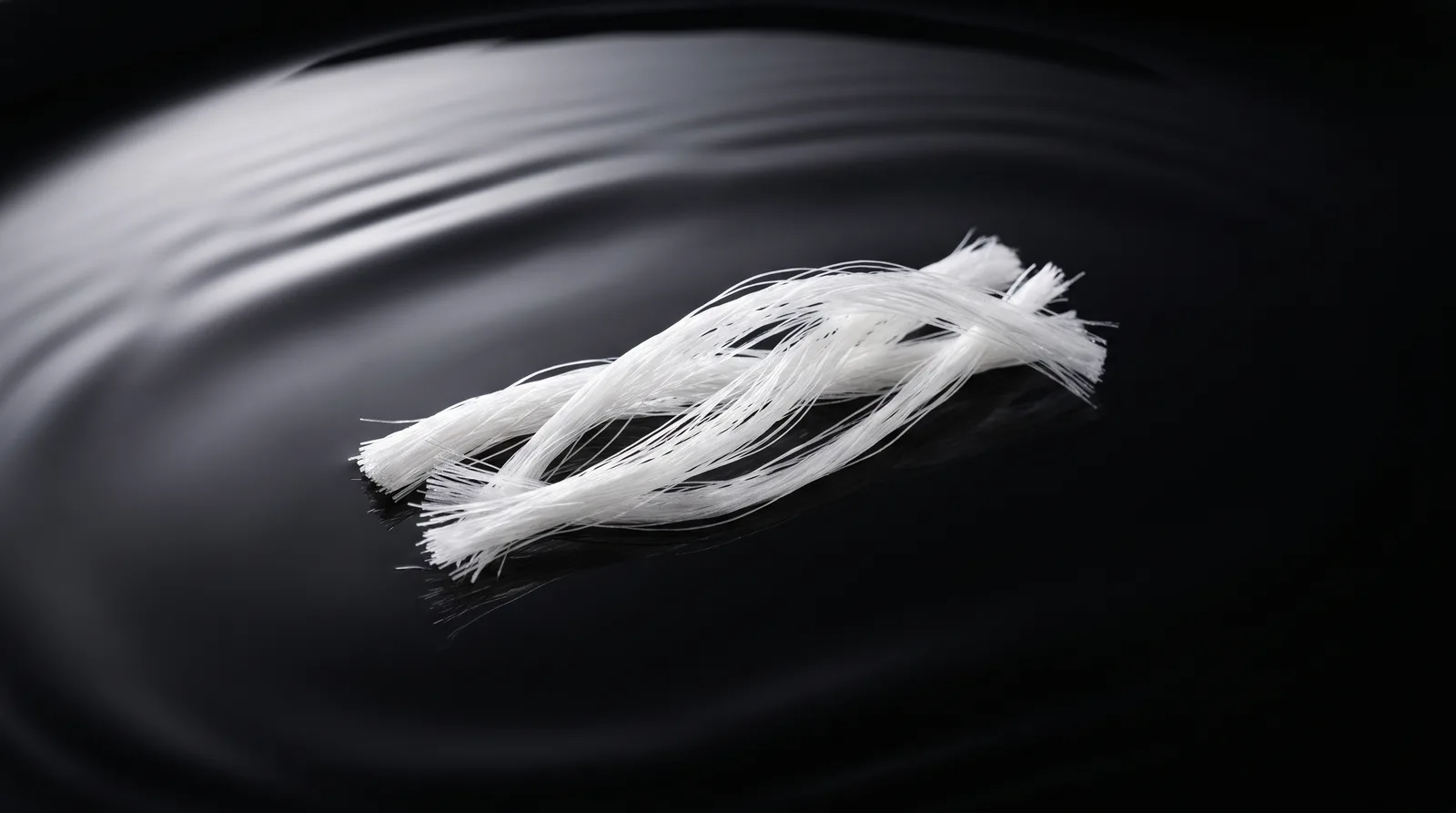 Twisted white fibrous Sodium DNA biopolymer strands on a polished black obsidian surface